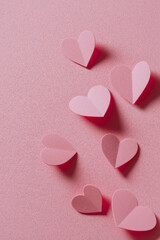 Pink paper hearts scattered across a textured pink surface, creating a whimsical, loving, and visually appealing arrangement.