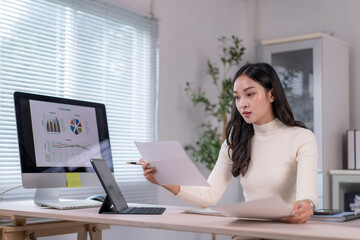 Businesswoman analyzing financial reports and charts on computer and documents at office desk