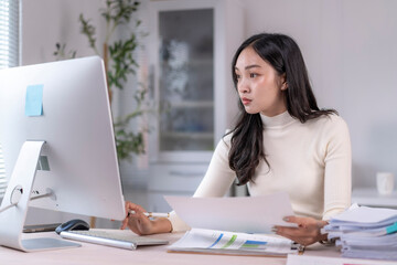Focused asian businesswoman working with computer and documents at office desk