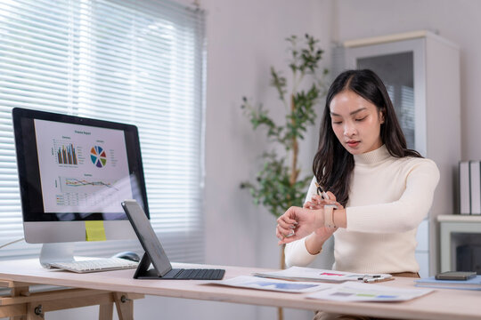 Businesswoman using smart watch in office with charts on computer screen