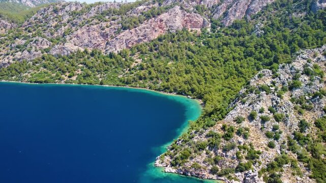 aerial perspective captures the beauty of Cennet Koyu, also known as Paradise Bay, in Turkey. Crystal clear turquoise waters meet a pristine coastline framed by vibrant green, pine covered hills and r