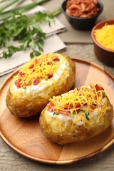 Tasty baked potatoes with sour cream, green onion, cheese and bacon on wooden table, closeup