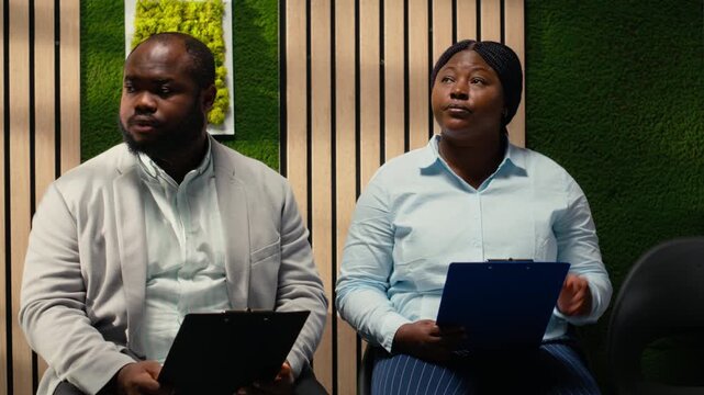 Anxious black woman job seeker getting called in the HR office to start interview, awaiting discussion and showcasing anticipation in office. People preparing for the recruitment process. Camera B.