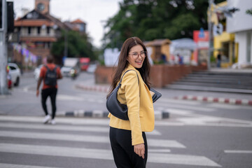 Fototapeta premium Smiling businesswoman crossing city street holding tablet and looking over shoulder