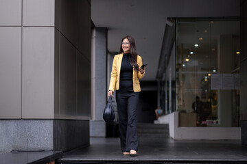 Smiling businesswoman walking and using smartphone in urban setting