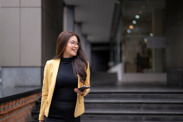 Smiling businesswoman holding smartphone walking outside office building