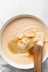Overhead of moi moi mixture in a white ceramic bowl, top view of nigerian bean pudding being mixed, process of making nigerian moi moi