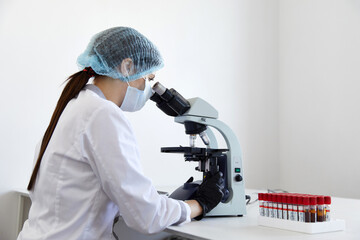 Female scientist looking through microscope in modern chemical laboratory doing some research. Analyzing blood samples using a microscope