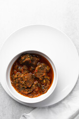 Overhead view of miyan taushe in a white bowl, top view of northern nigerian miyan taushe soup on a white countertop