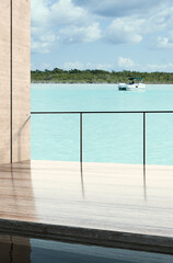 Modern luxury villa terrace with polished wooden floor and minimalist railing overlooking turquoise tropical lagoon, white yacht, and green coastline under partly cloudy sky.