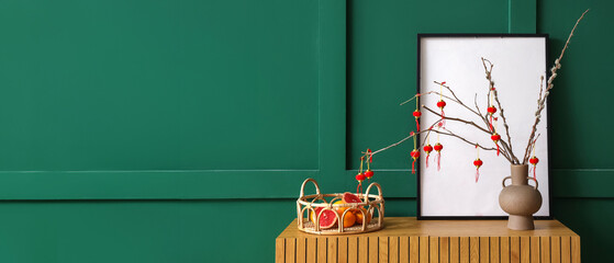 Wooden cabinet with tree branches, decorative Chinese lanterns and fruit basket near green wall....