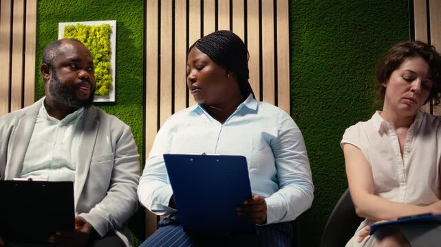 Confident job applicants sitting in the hallway before hiring interview, reviewing their CVs and preparing for employment questions with HR recruiters during a talent acquisition meeting. Camera A.