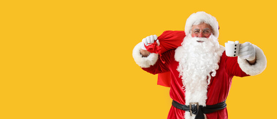 Santa Claus with Christmas bag and cup of cacao on yellow background