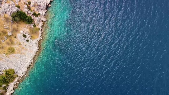beauty of Cennet Koyu, also known as Paradise Bay, in Turkey, captured from an aerial perspective. This stunning footage showcases the pristine turquoise waters meeting the rugged, rocky coastline, su