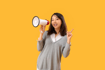 Beautiful Asian woman with megaphone pointing at something on yellow background. Dialogue concept