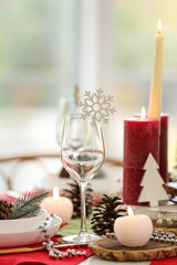 Christmas table setting with burning candles and fir cones in room, closeup