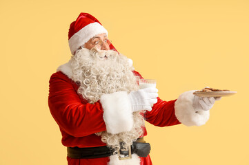 Santa Claus with glass of milk and cookies on yellow background