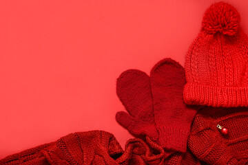 Warm mittens, hat and scarf on red background