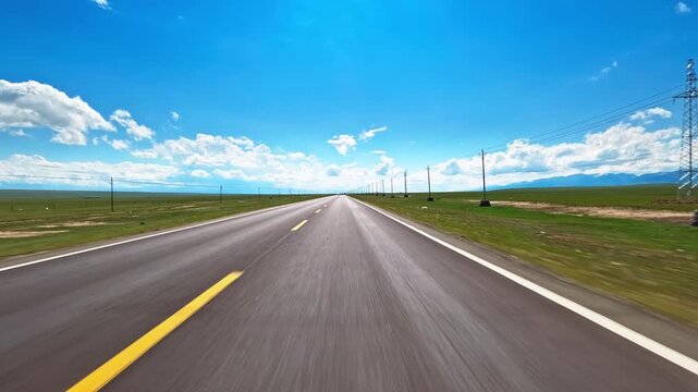 A fast car driving on an empty asphalt highway through vast green grasslands under blue sky