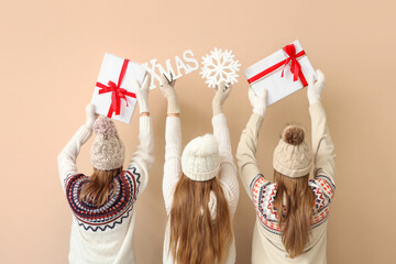 Women in warm clothes holding gift boxes and Christmas decor on beige background