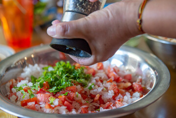 Una mano poniendo pimienta molida a un tazon con preparacion de SALSA BANDERA o PICO DE GALLO para...