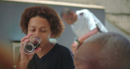 Young boy sipping soda from a glass during a casual outdoor lunch, enjoying the refreshing drink...