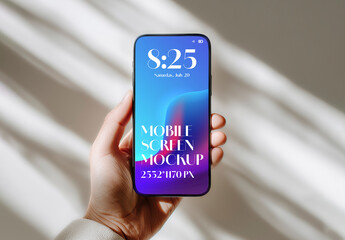 Hand holding a modern smartphone with a blank screen for a mockup against a wall with window shadows