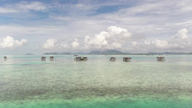 Aerial view of sea gypsy village over clear turquoise waters in Awan Biru Island Semporna, Sabah, Malaysia. Scenic seascape with coral reefs, coastal village, and blue tropical sky.