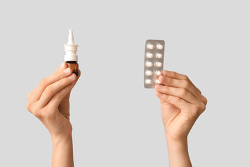 Female hands with bottle of nasal spray and pills on white background