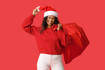 Beautiful young happy African-American woman with Santa bag on red background