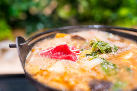 A steaming pot of Japanese sukiyaki with thinly sliced beef, tofu, vegetables, enoki mushrooms, and udon noodles.