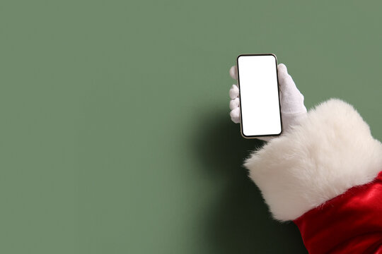 Santa hand with modern mobile phone against green background, closeup