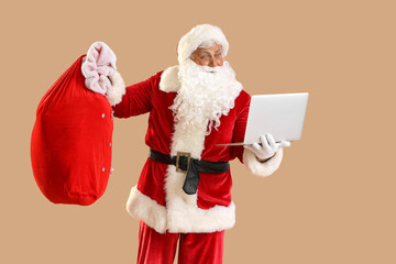 Shocked Santa Claus with Christmas bag and laptop on beige background