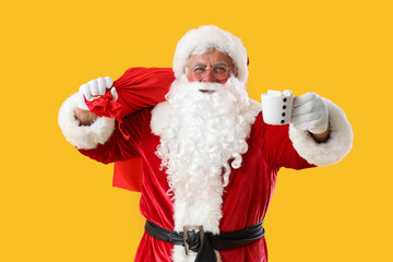 Santa Claus with Christmas bag and cup of cacao on yellow background