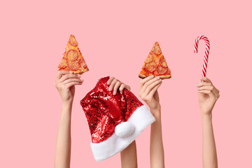 Female hands with pizza slices, Santa hat and candy on pink background
