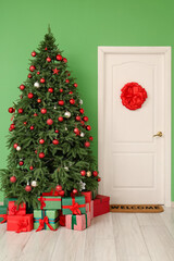 Interior of hallway with decorated door, gift boxes and Christmas tree near green wall