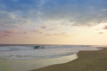 Colores tenues del atardecer cerca de la orilla del mar con algunas olas en movimiento.