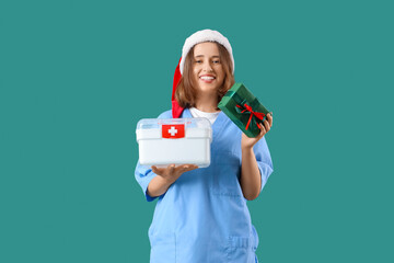 Female doctor with Santa hat, gift and first aid kit on green background