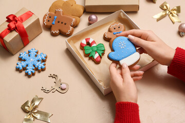 Female hands with gift box of sweet gingerbread cookies and Christmas decorations on beige background