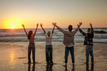 Fototapeta premium Friends raising arms enjoying golden sunset at beach