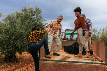 Farmers helping colleague climb onto trailer in olive grove