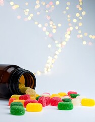 Assorted gummy candies spilled from a brown bottle against a blurred background of golden lights