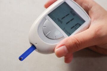 Close-up of a hand holding a blood glucose meter with test strips. A portable medical device for diabetes screening and health monitoring. A digital glucometer used to test blood sugar levels.