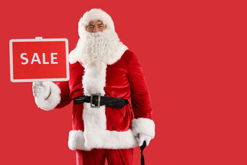 Santa Claus holding board with word SALE on red background. Christmas celebration