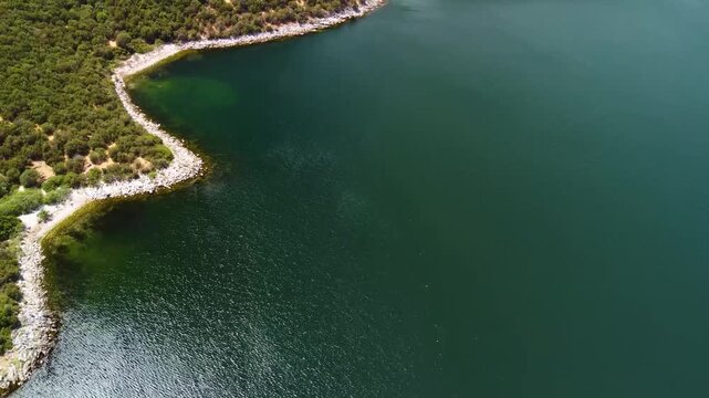 An aerial drone shot captures the stunning, tranquil waters of Bafa Lake in Turkey, showcasing its unique, winding coastline and the lush, rocky shorelines covered with Mediterranean vegetation.