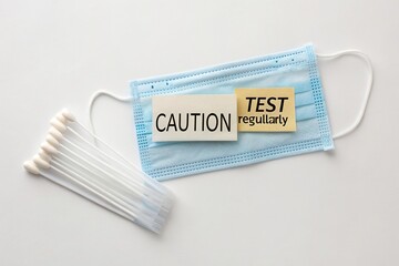 Medical mask with caution sign and test reminder alongside cotton swabs for health awareness