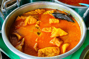 A pot of Indonesian curry with tofu pieces simmered in rich coconut milk and turmeric-based spices, creating a savory and vibrant golden-yellow dish.