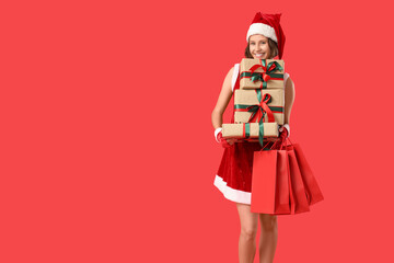 Beautiful young happy woman in Santa costume with gift boxes and shopping bags on red background. Christmas celebration