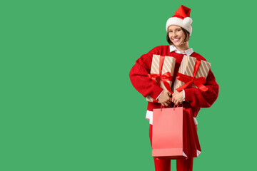 Beautiful young happy woman in Santa hat with shopping bags and gift boxes on green background. Christmas celebration