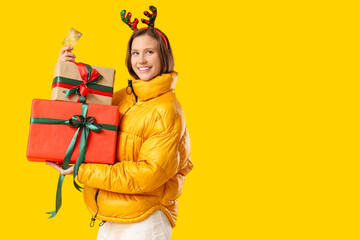 Beautiful young happy woman in reindeer horns with gift boxes and credit card on yellow background. Christmas celebration